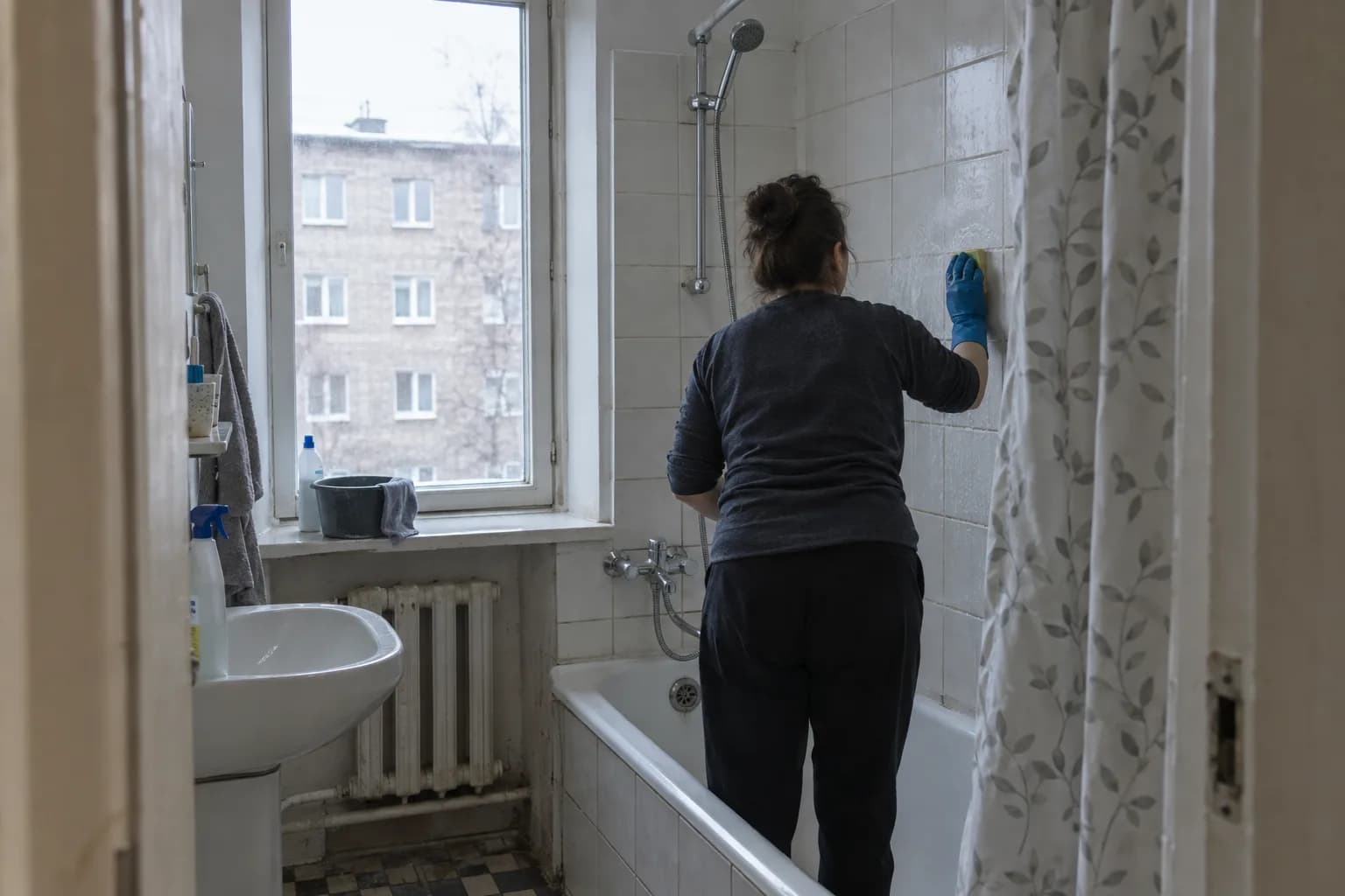 Koristaja küürib väikese vannitoa plaatseina vanemas telliskortermajas