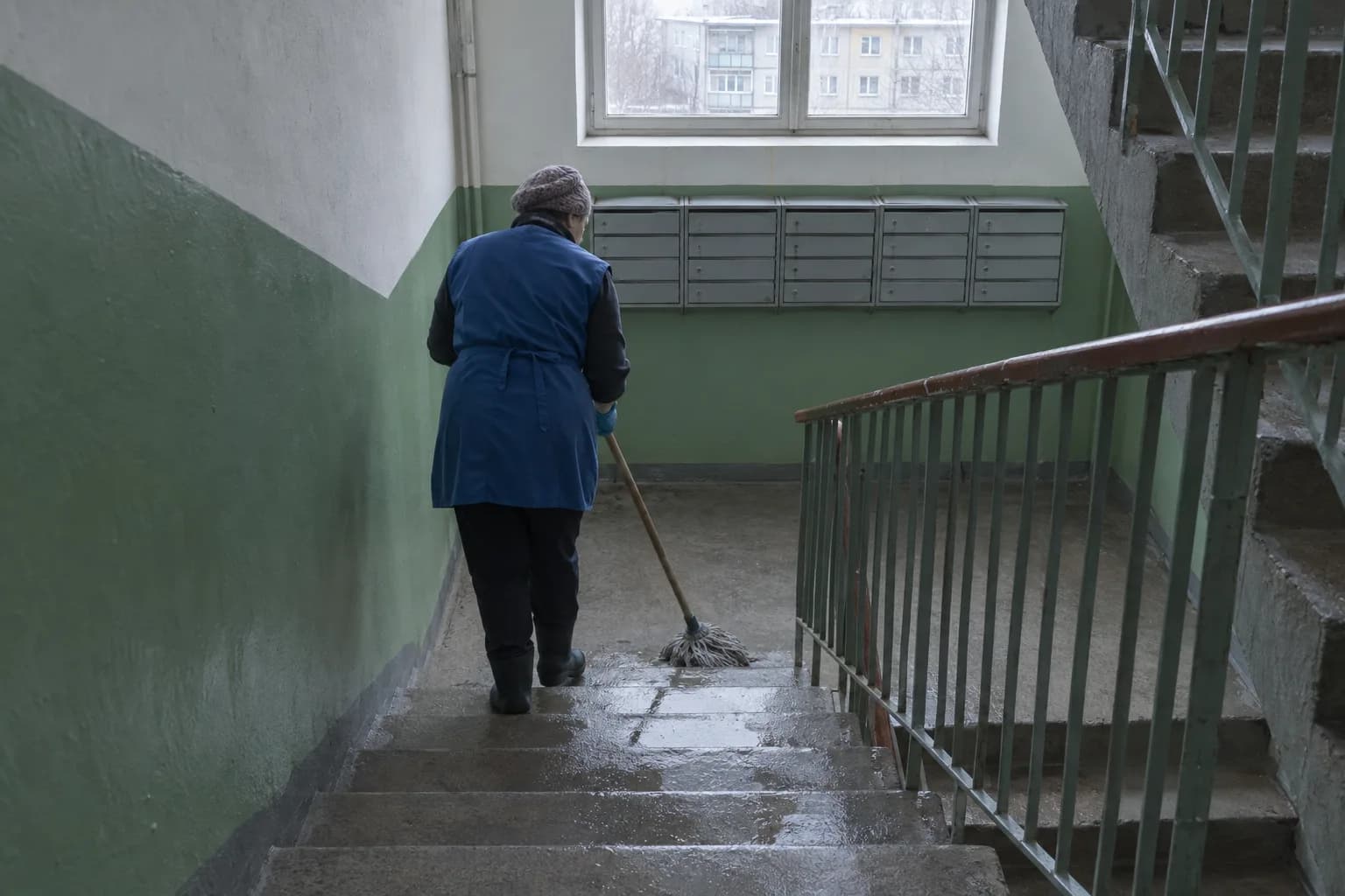 Koristaja peseb kortermaja trepikoja betoonist astmeid, seinal on postkastid